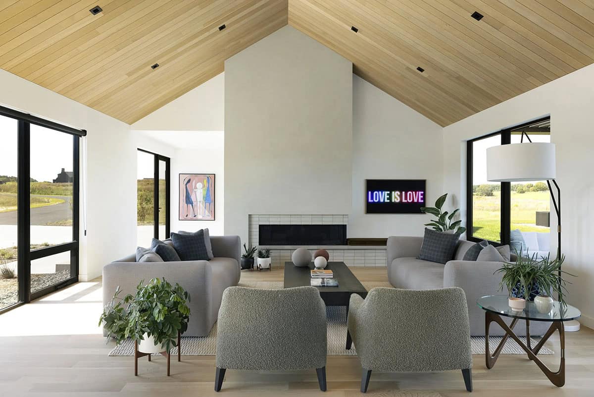 Symmetrical living room with two gray sofas, boucle chairs and a linear fireplace under a vaulted white oak ceiling, with windows on both sides
