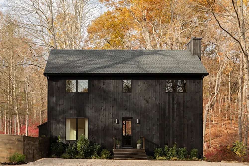 Dark charred-timber house with a gabled roof and chimney, surrounded by autumn woods