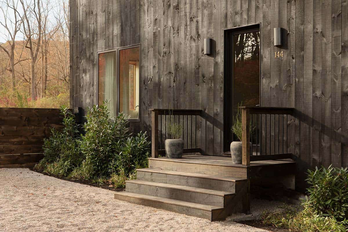 Front entry with a small wood stoop, black door, wall sconces, and the house number 144