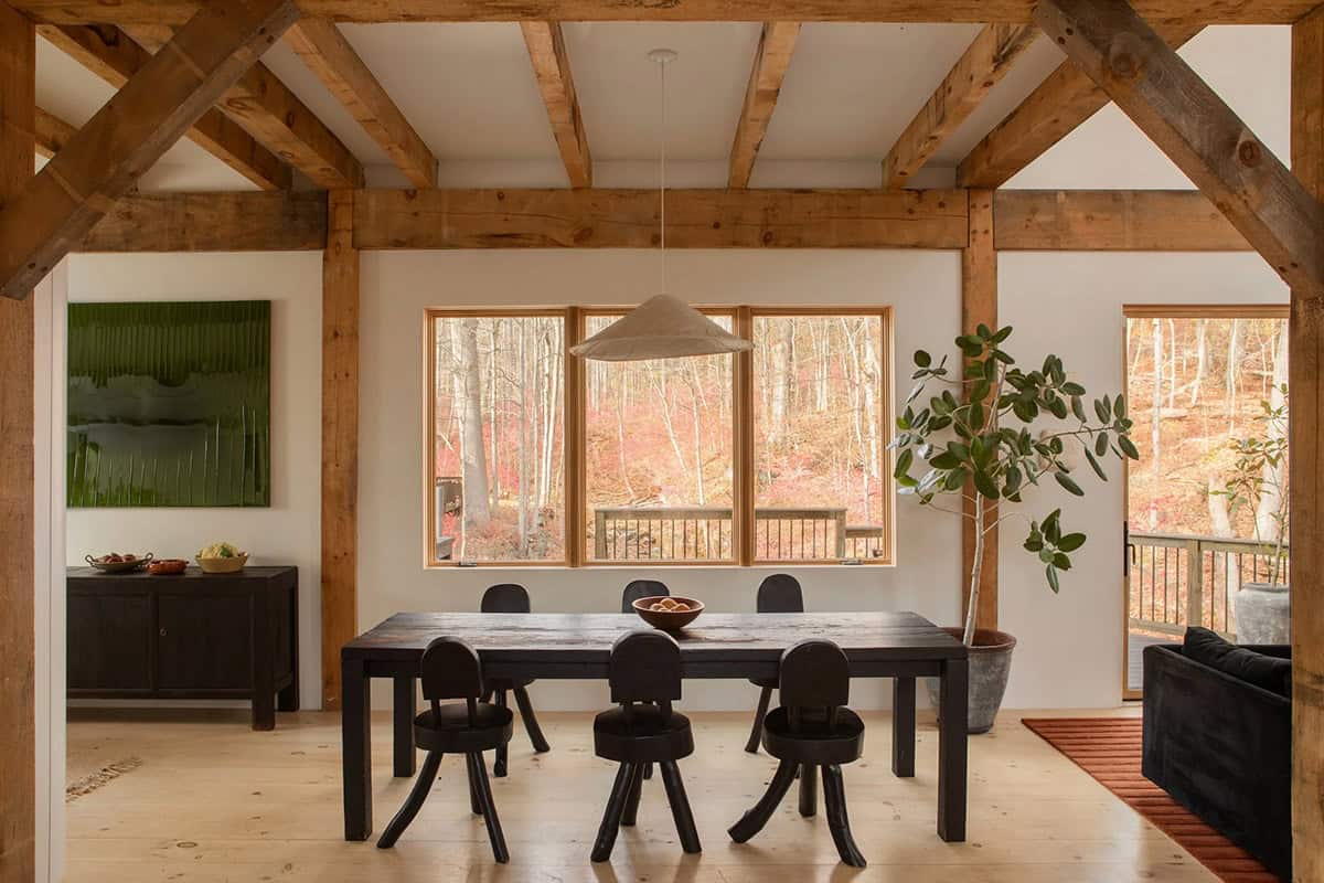 Dining room with exposed timber beams, a black wood table, and large windows onto the woods