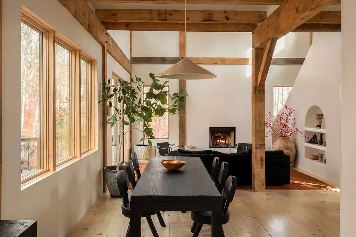 Open living and dining space with timber frame, pale plank floors, and a fireplace in the background
