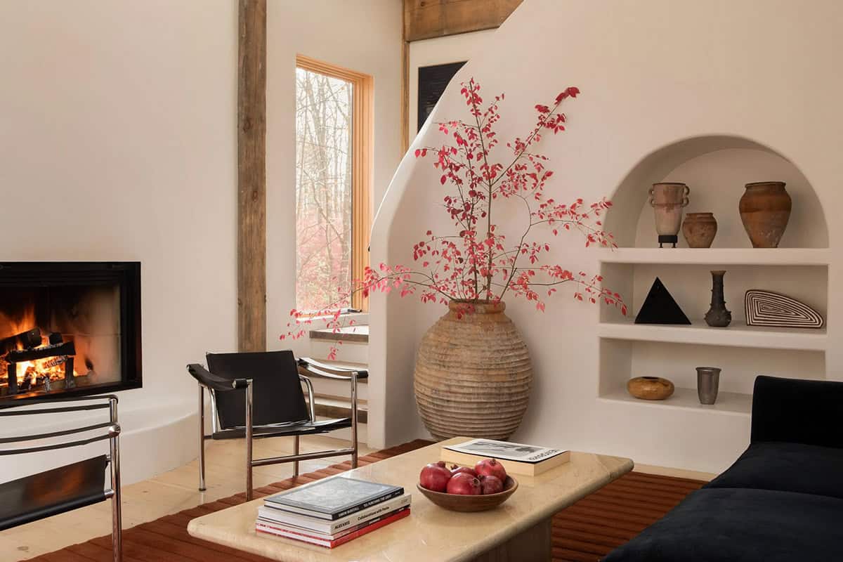 Living room corner with a large terracotta urn of red branches beside an arched plaster niche with pottery