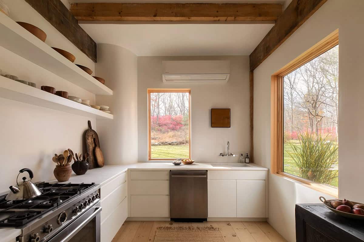 Galley kitchen with white cabinetry, open shelves of wooden bowls, a gas range, and windows to the lawn