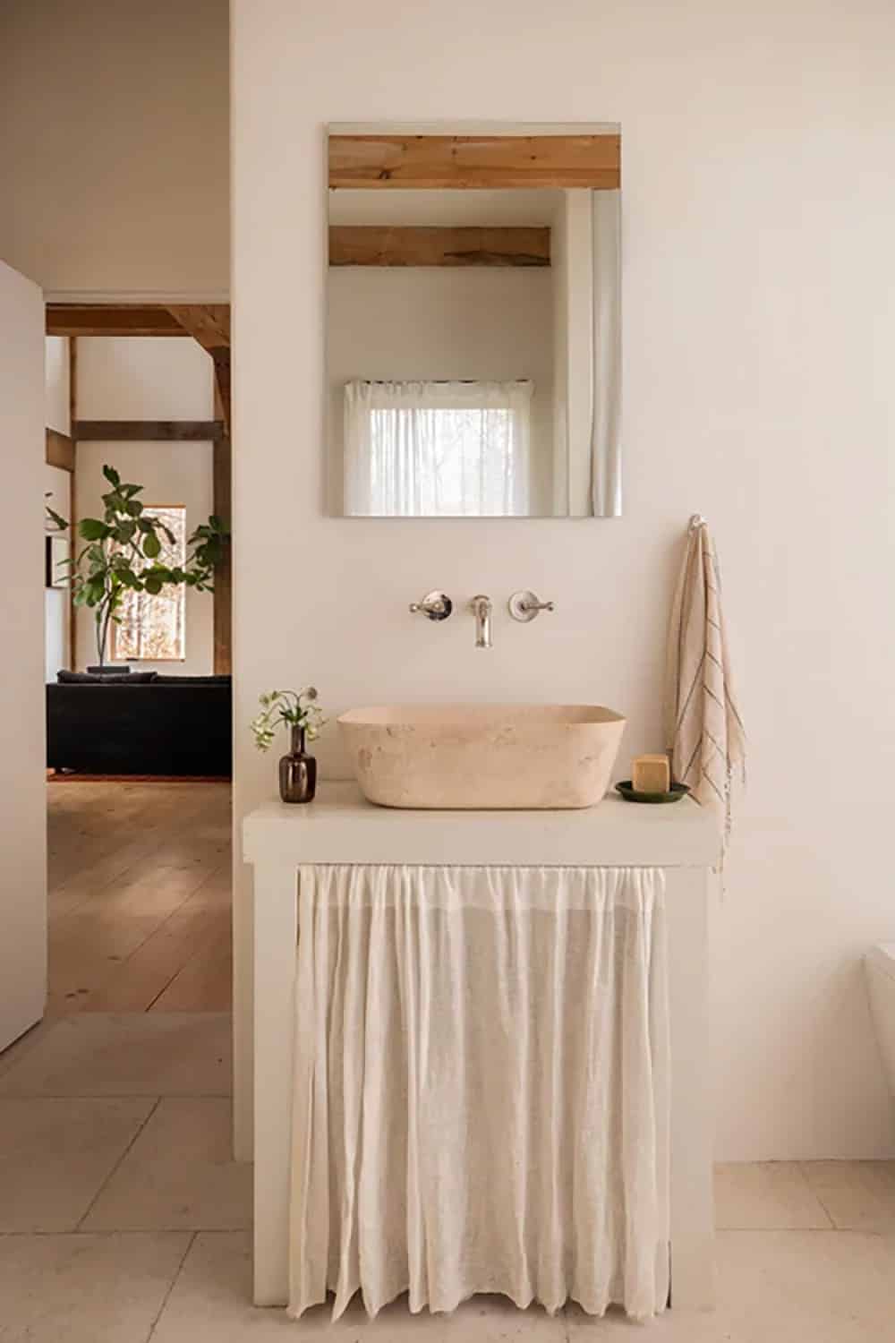 Bathroom vanity with a stone vessel sink, linen skirt, and wall-mounted faucet, with a view into the living room
