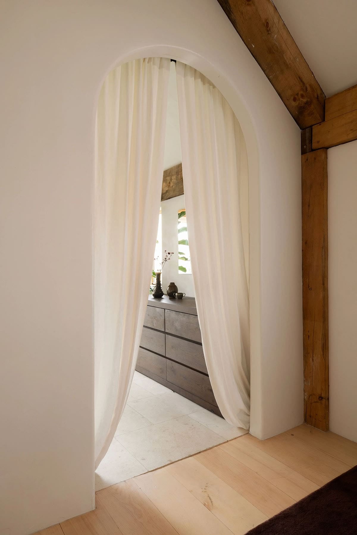Arched doorway with a sheer cream curtain opening to a stone-floored bathroom