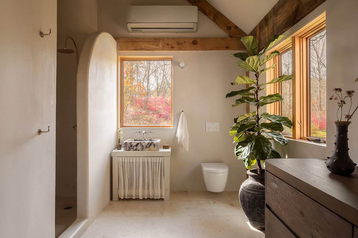 Bathroom with a marble vessel sink, wall-hung toilet, arched shower wall, and a fiddle-leaf fig by large windows