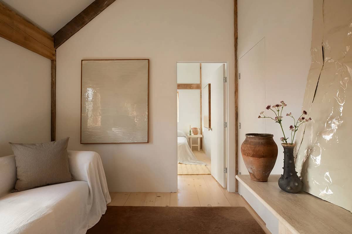 Sitting nook with a linen-draped sofa, glossy cream artwork, and a view through a doorway into a bedroom
