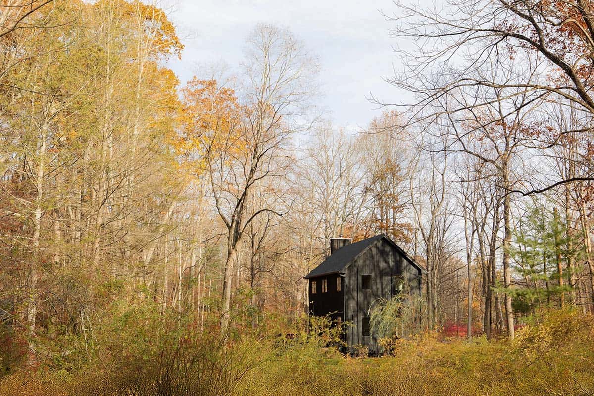 Dark house tucked among golden trees and shrubs, seen from a distance