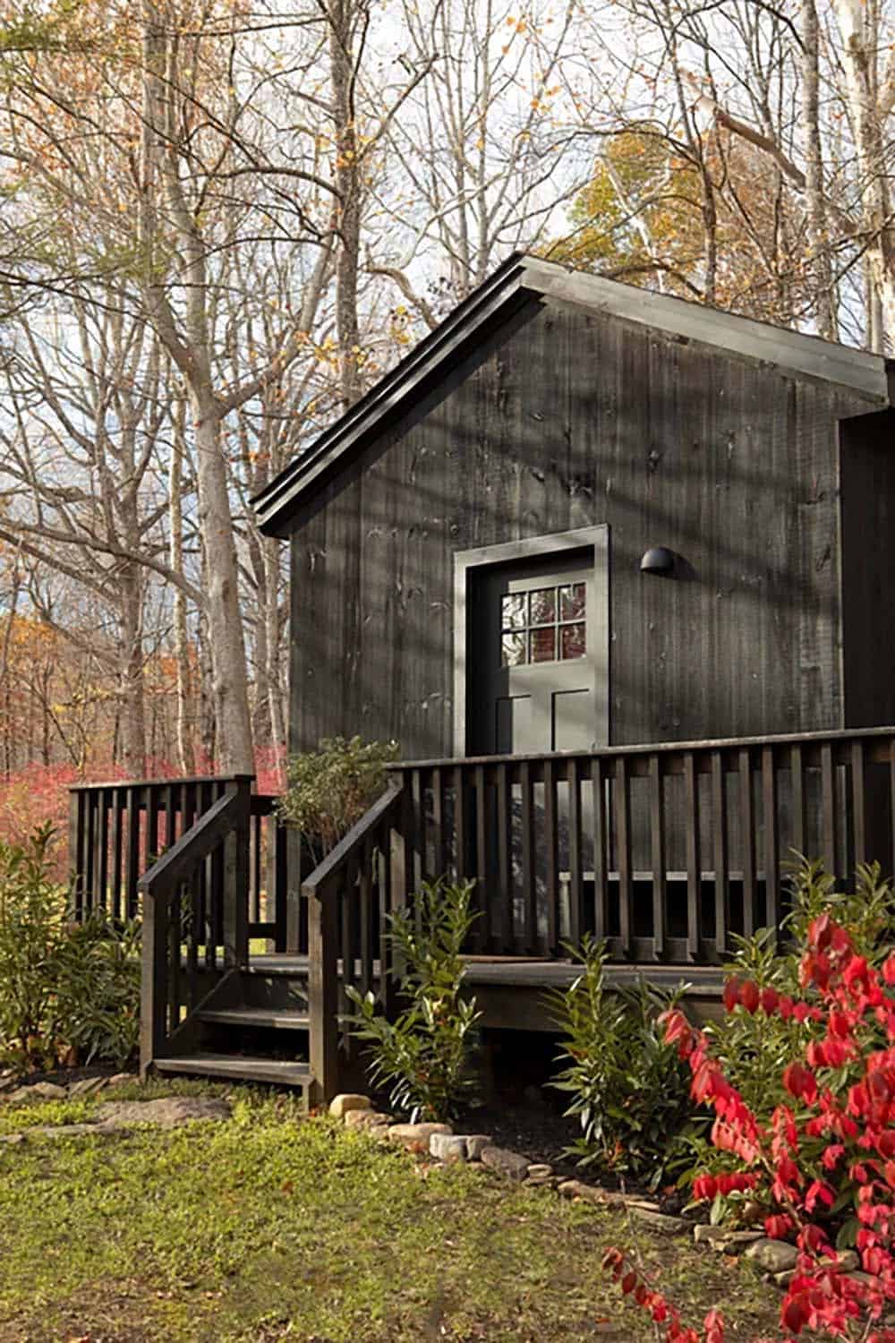 Small black cabin with a covered porch, railed steps, and a glass-paned door