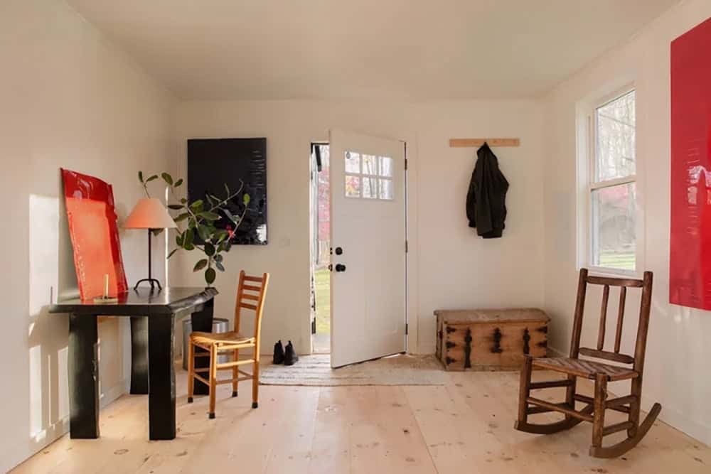 Cabin entry with a white door, black console table, red artwork, a trunk, and a rocking chair