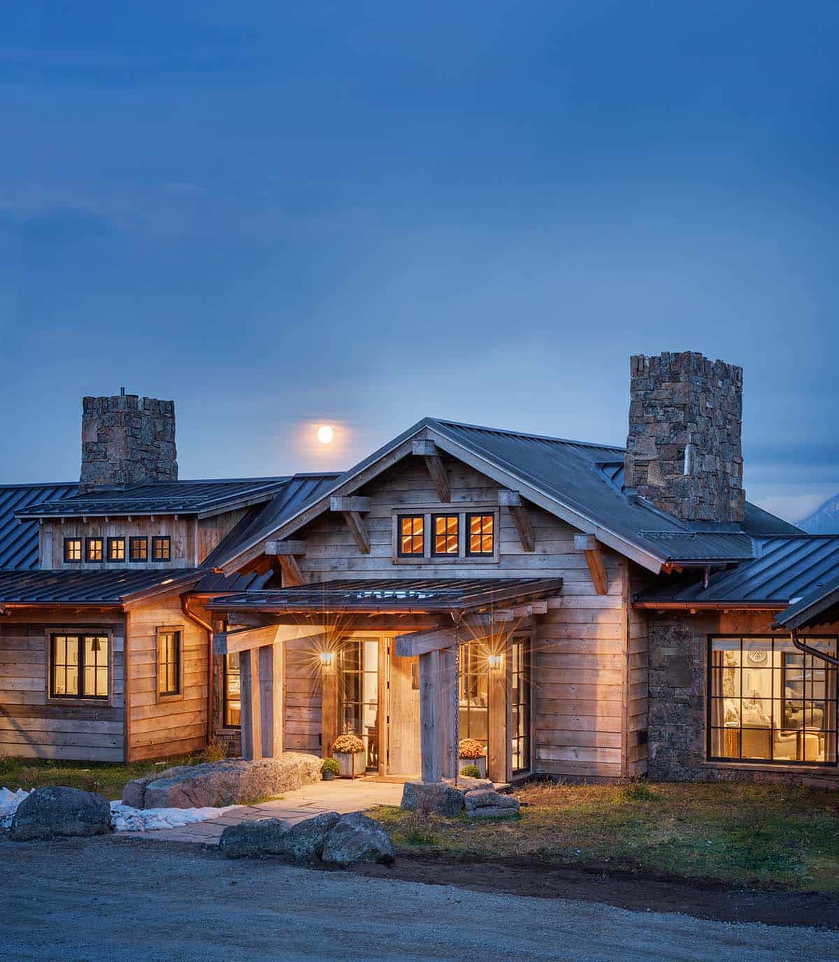 Ranch home front porch glowing at twilight with a full moon rising between two stone chimneys