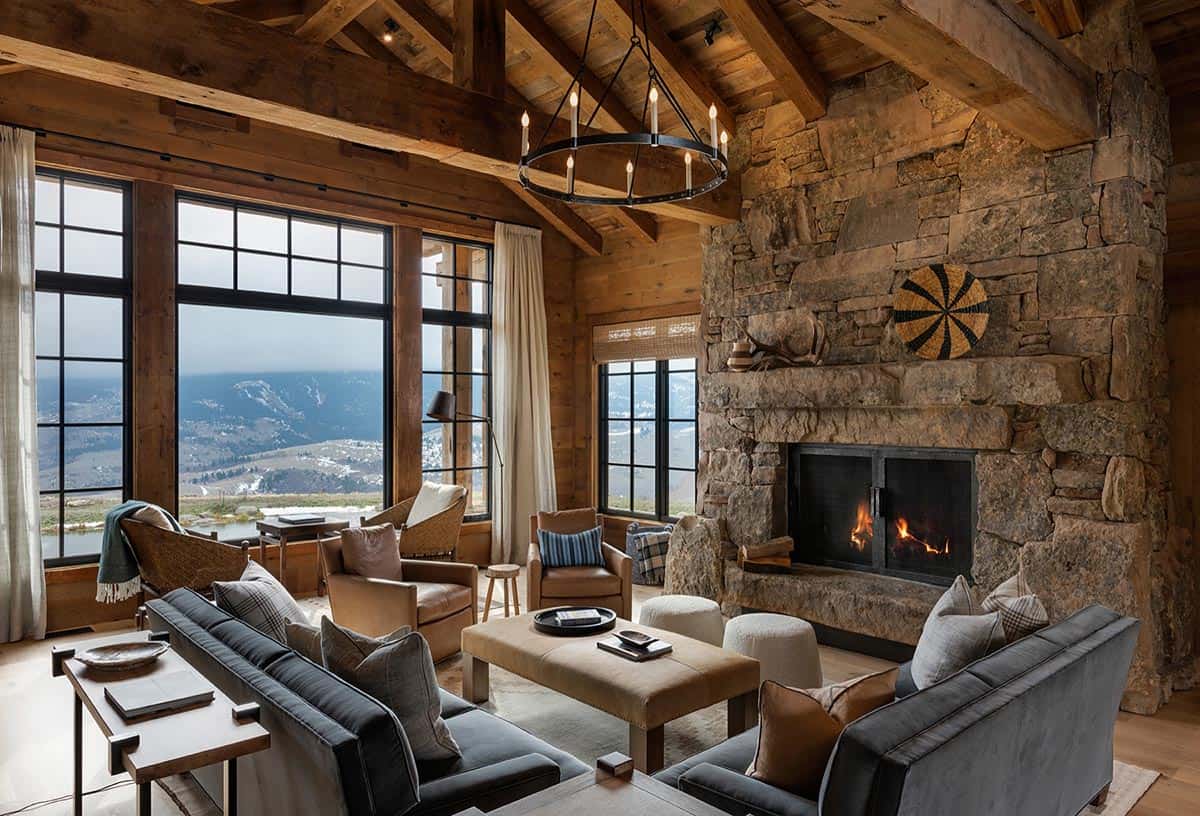 Living room with a floor-to-ceiling stone fireplace, iron ring chandelier, gray sofas and large windows framing mountain views