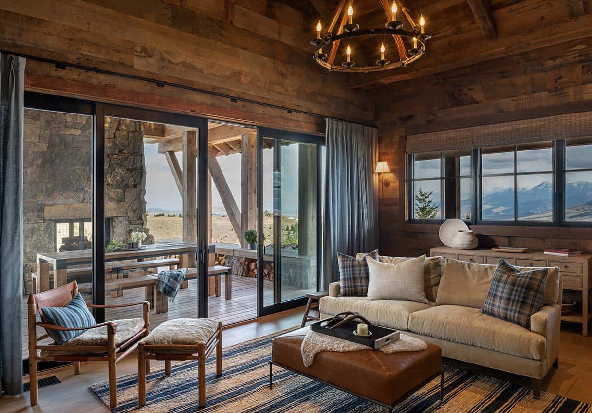 Den with reclaimed wood walls, a candle chandelier and sofa, with sliding glass doors opening to a covered porch and outdoor fireplace