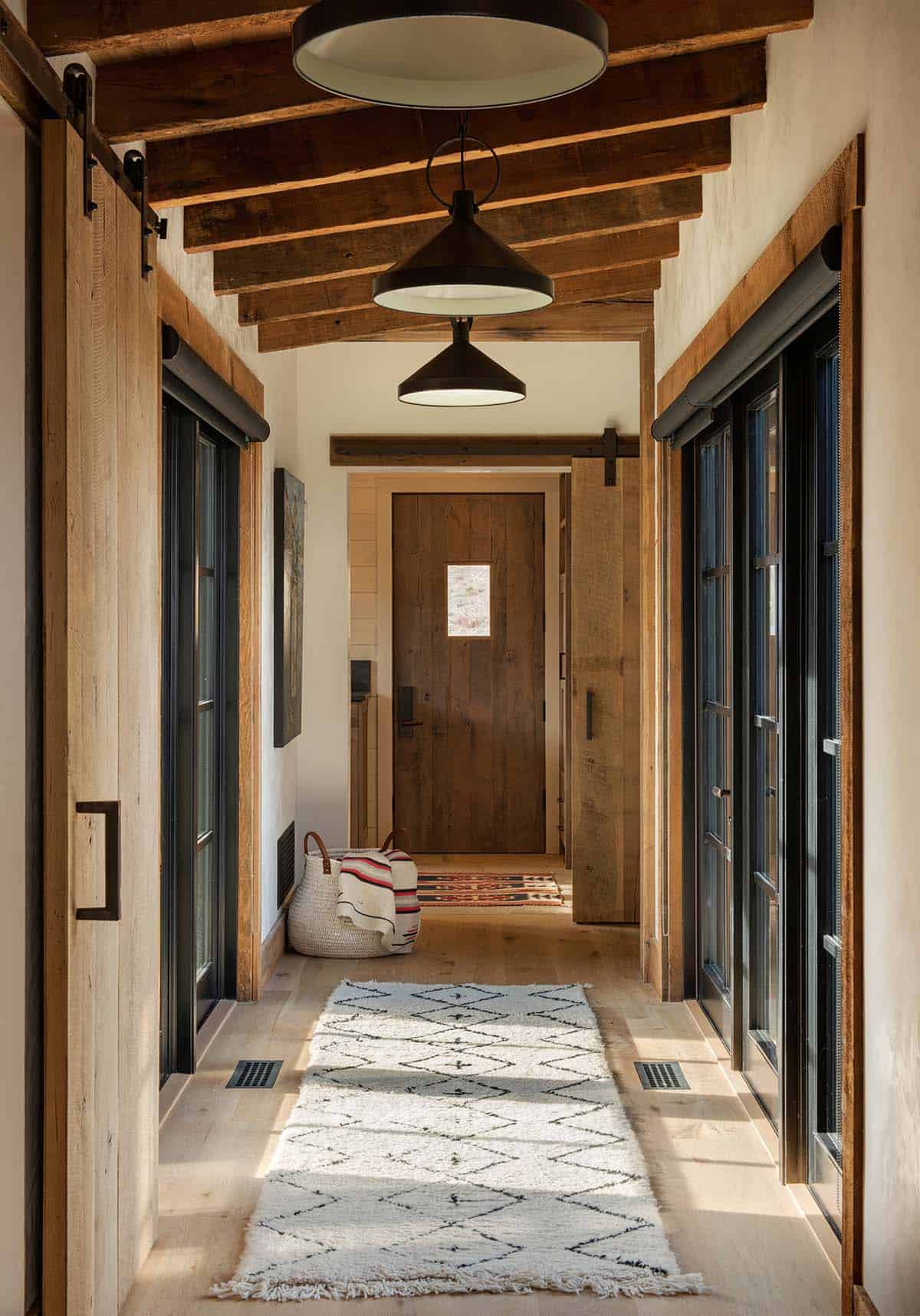 Hallway lined with black-framed glass doors and sliding barn doors under a beamed ceiling with black pendant lights and a shag runner