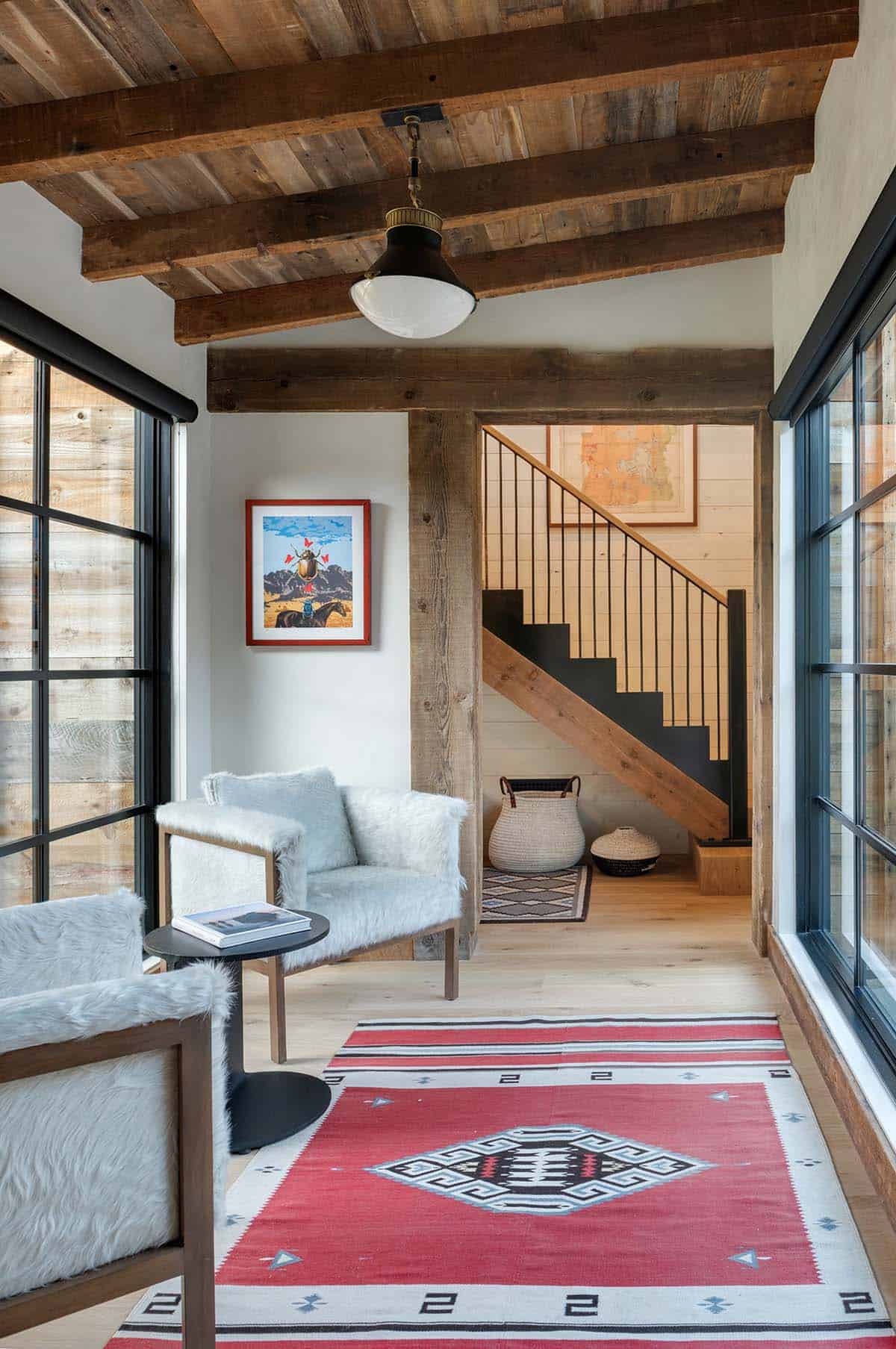 Sitting area with white faux-fur chairs and a red Southwestern rug, opening to a staircase with a black spindle railing
