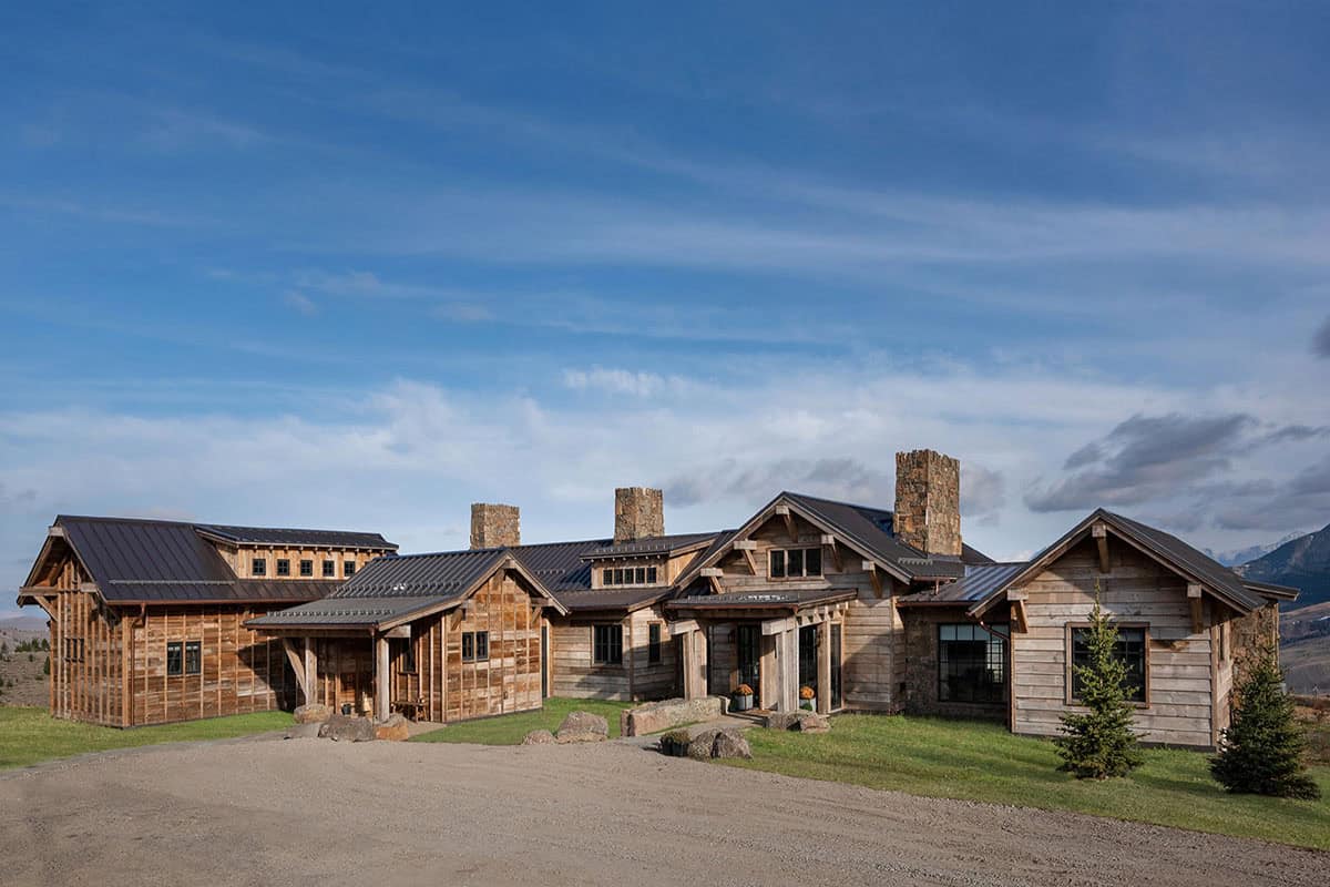 Ranch home exterior with reclaimed wood siding, metal roofs and three stone chimneys under a blue sky