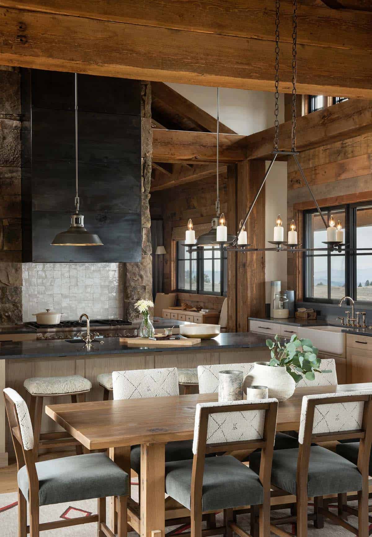Dining table with patterned upholstered chairs in front of a kitchen island, handmade tile backsplash and black steel range hood