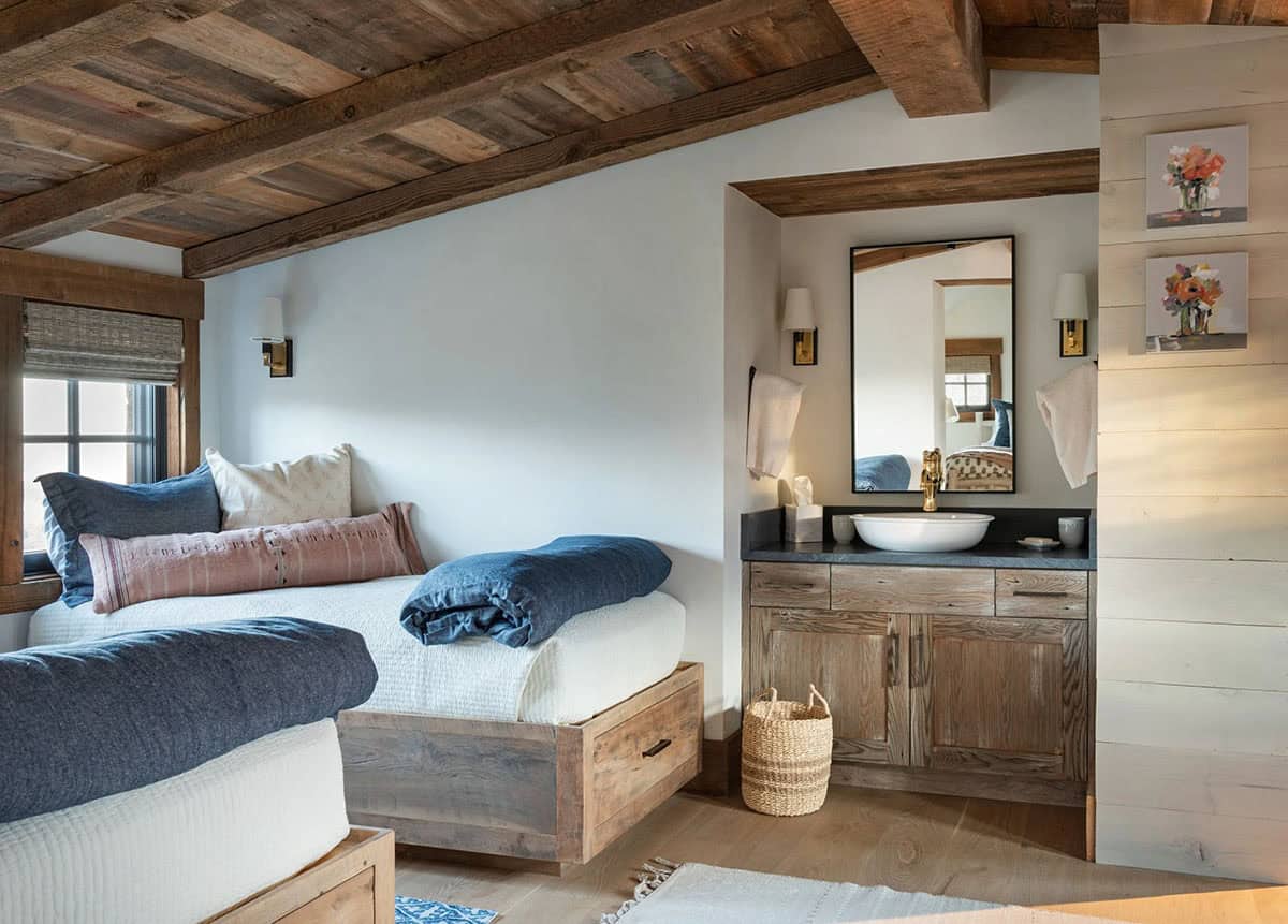 Loft guest room with twin beds on wood drawer bases under a beamed ceiling, beside a vanity nook with a vessel sink
