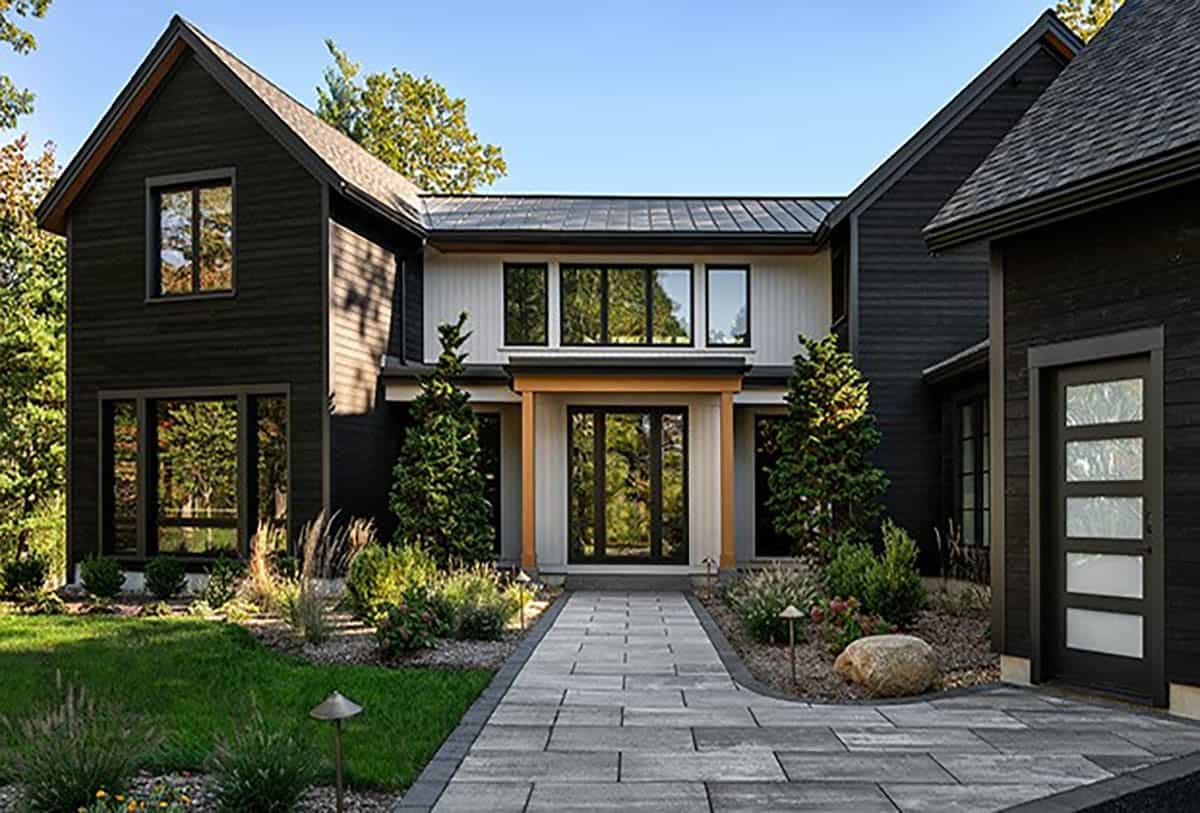Paver walkway through a planted courtyard to a glass front door between charred wood wings and the garage