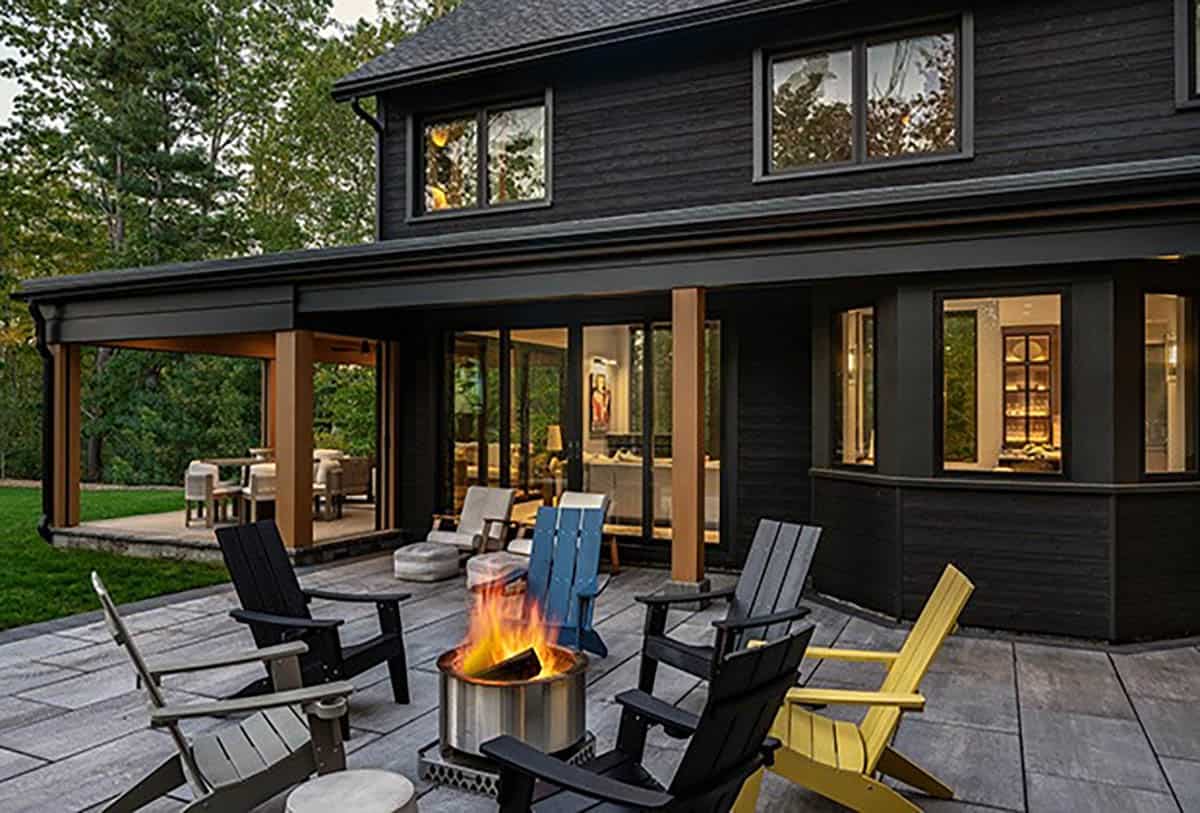 Colorful Adirondack chairs around a fire pit on a stone patio beside the covered porch