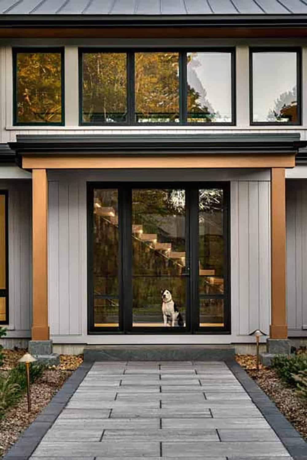 Cedar-post entry with a glass front door and a dog sitting inside at the foot of the floating staircase