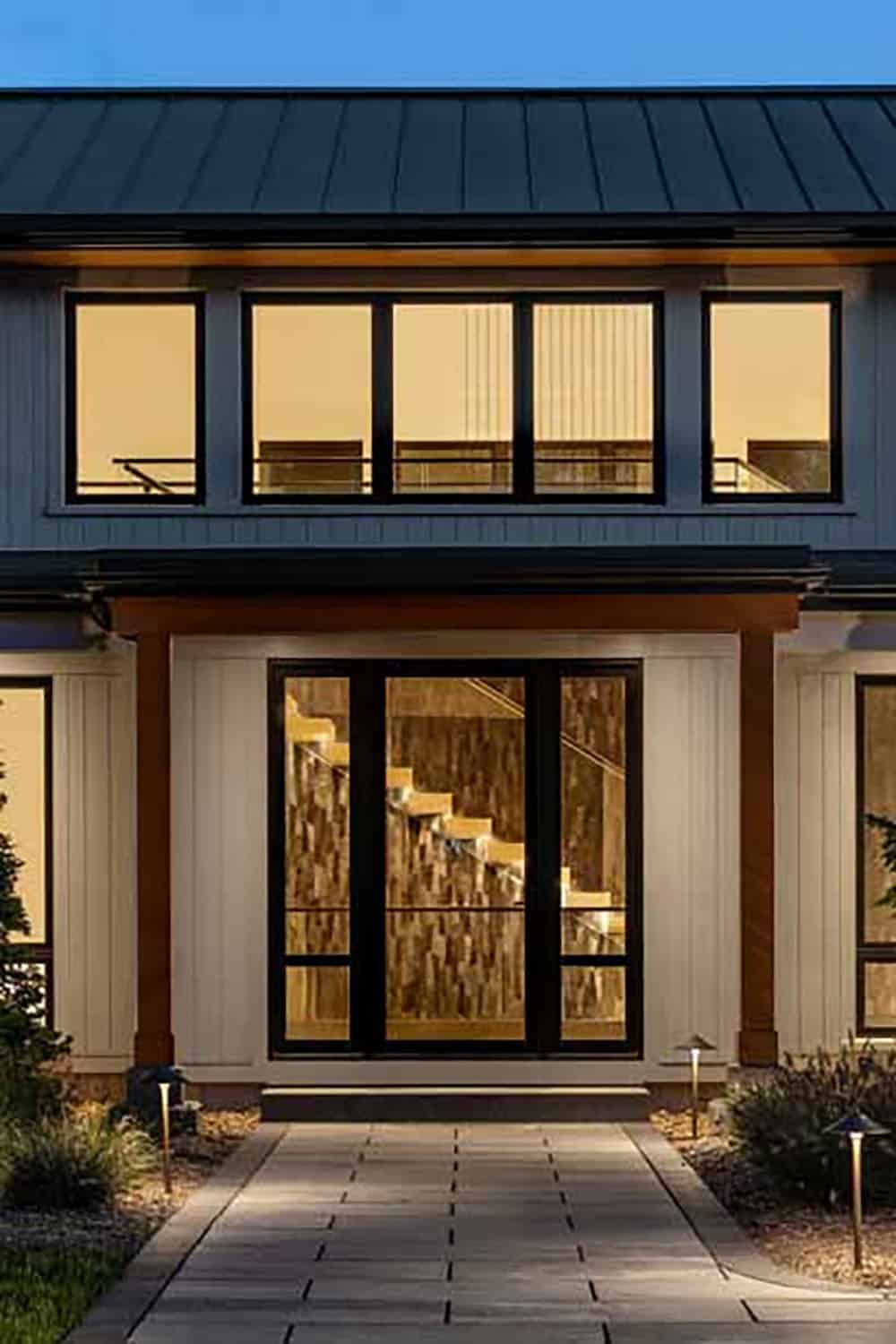 Front entry at dusk with clerestory windows above a glass door showing the lit floating staircase