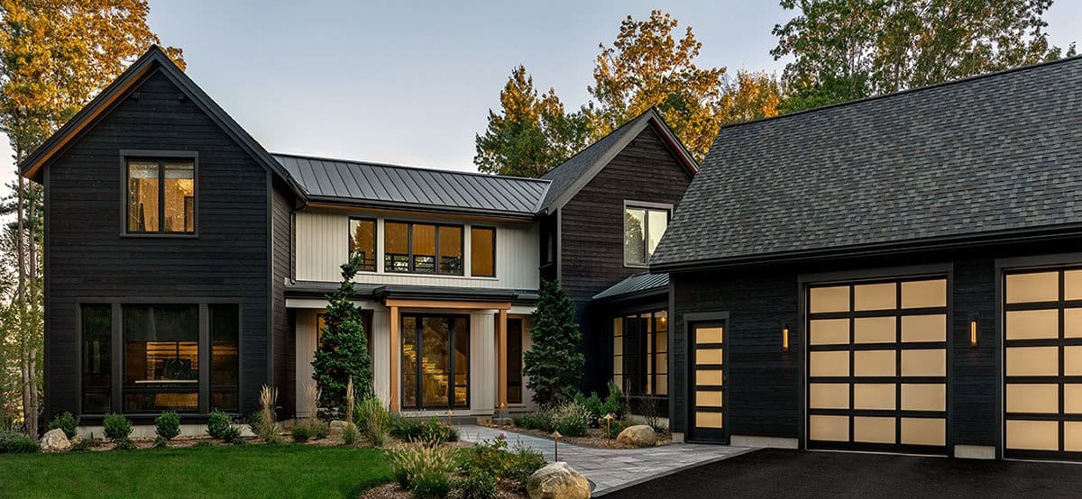 Front of the house at dusk with black charred-wood gables, a white board-and-batten entry, and a garage with frosted glass doors