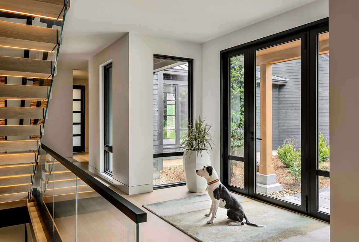Entry hall with a dog sitting on a rug by tall glass doors to the courtyard, beside the floating staircase