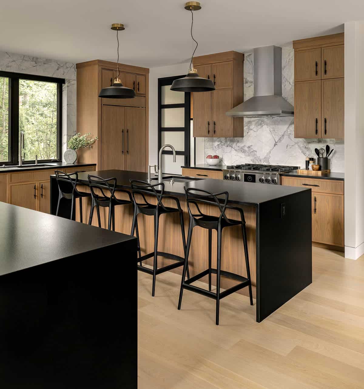Kitchen with walnut cabinets, a black waterfall island with black barstools, and a marble slab backsplash