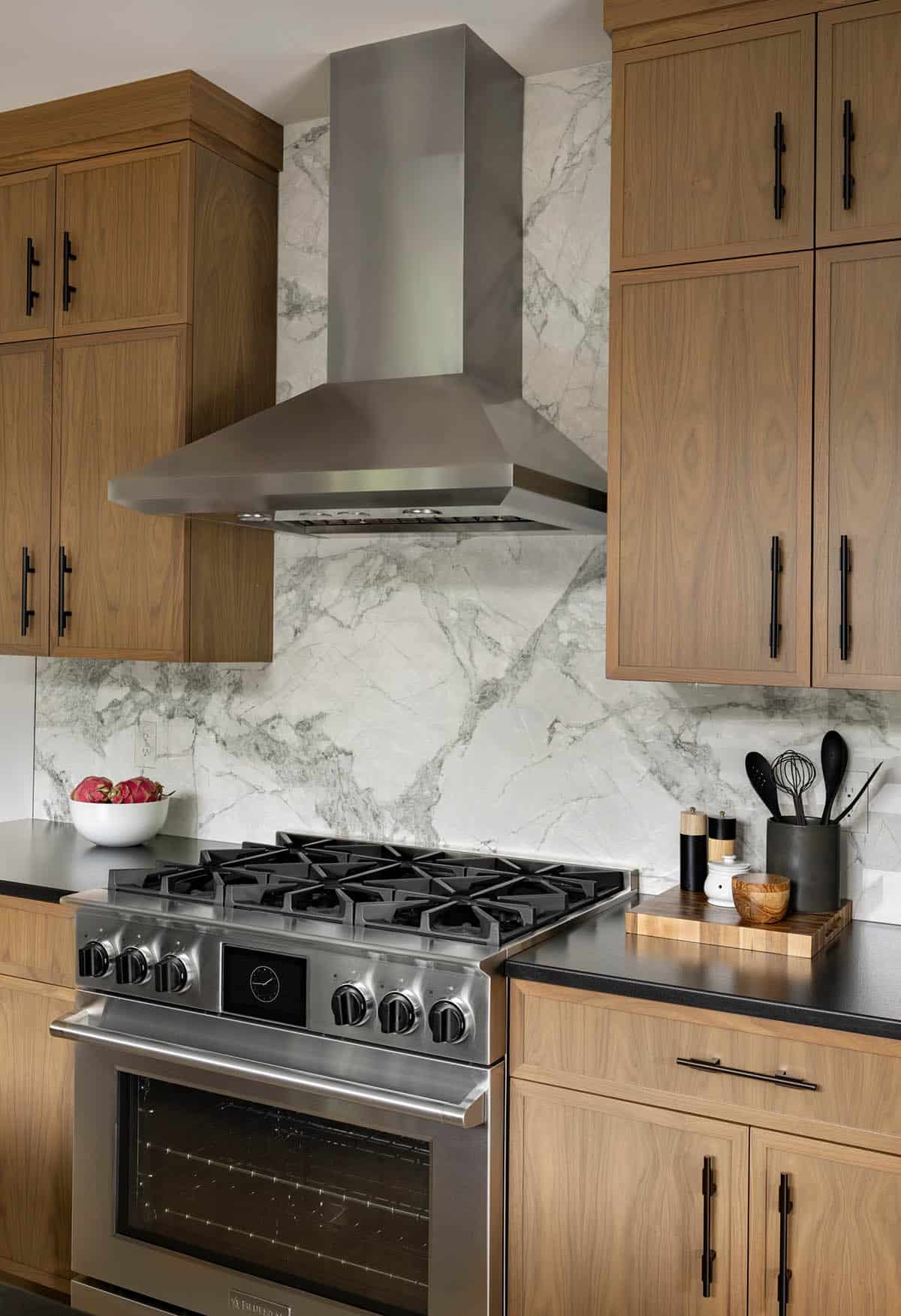Professional range under a stainless hood, with a marble slab backsplash and walnut cabinets