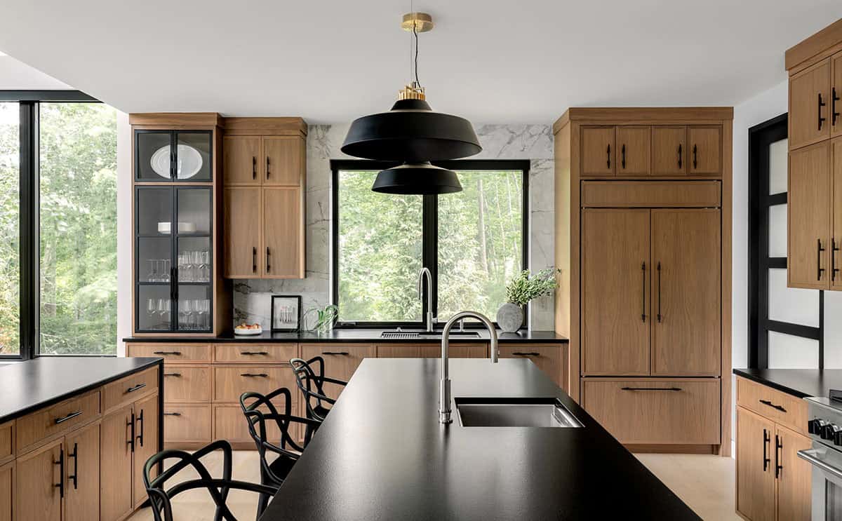 Black island with a sink under a black pendant, facing glass-front cabinets and a window to the trees
