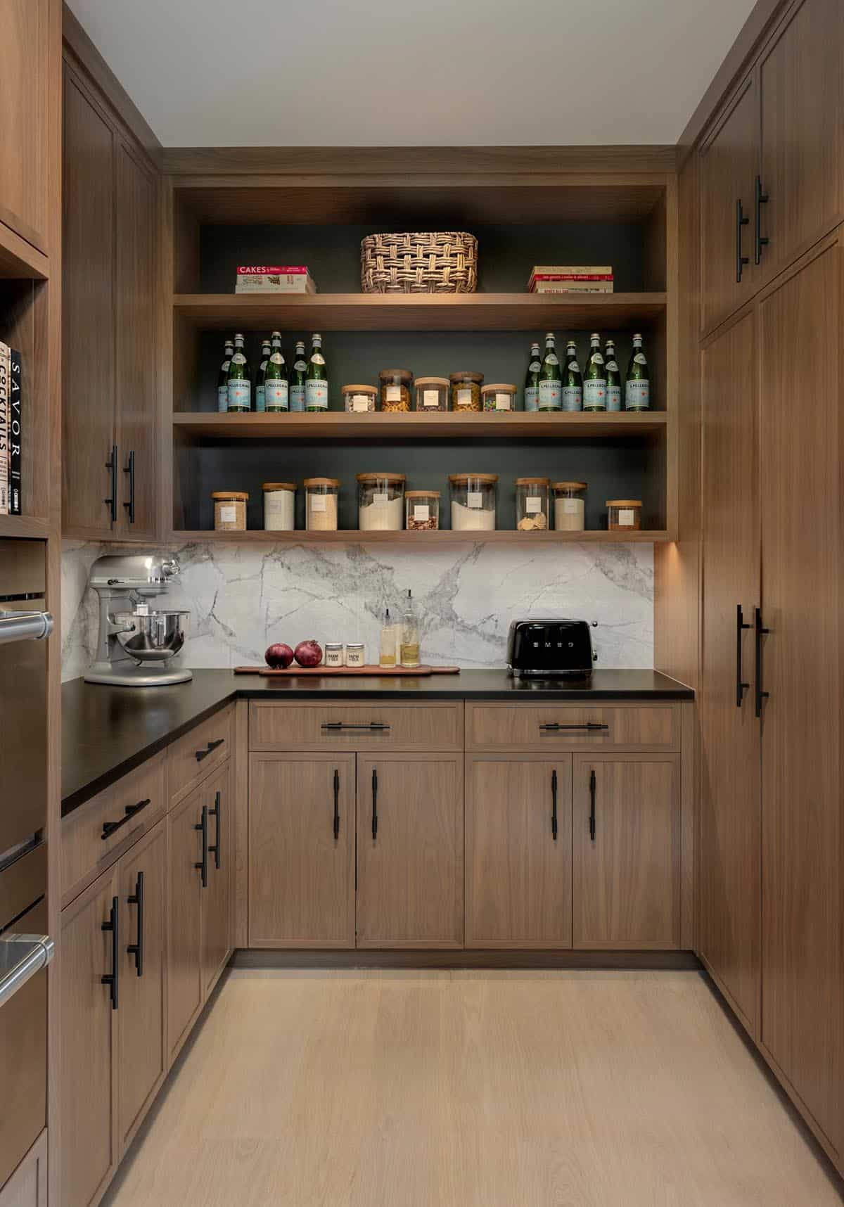 Walk-in pantry with walnut cabinets, open shelves of glass jars, and a marble backsplash
