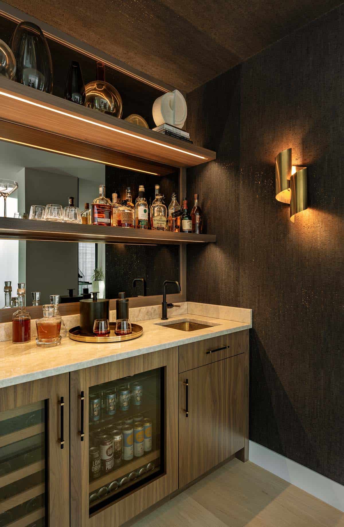 Wet bar with walnut cabinets, beverage fridges, a hammered brass sink, lit shelves, and a gold sconce