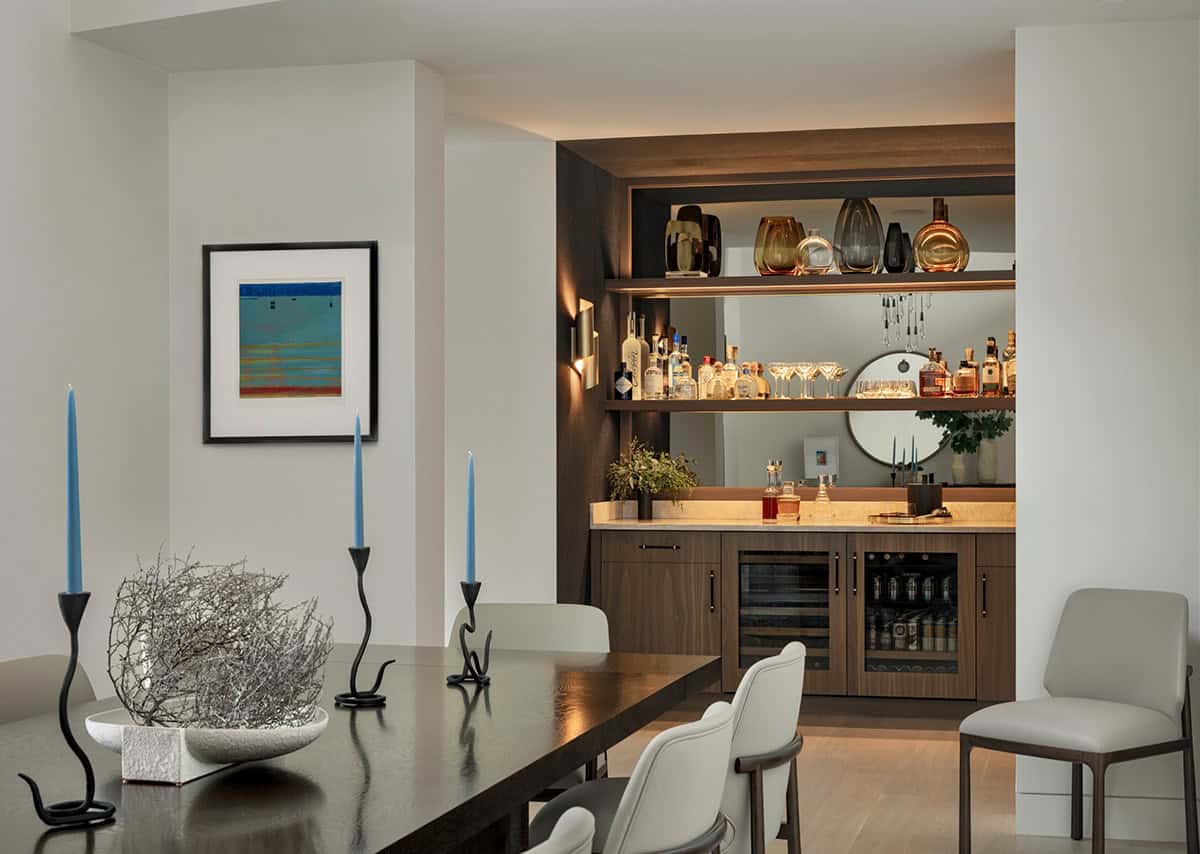 Dining table with blue taper candles, looking toward a lit wet bar with mirrored shelves