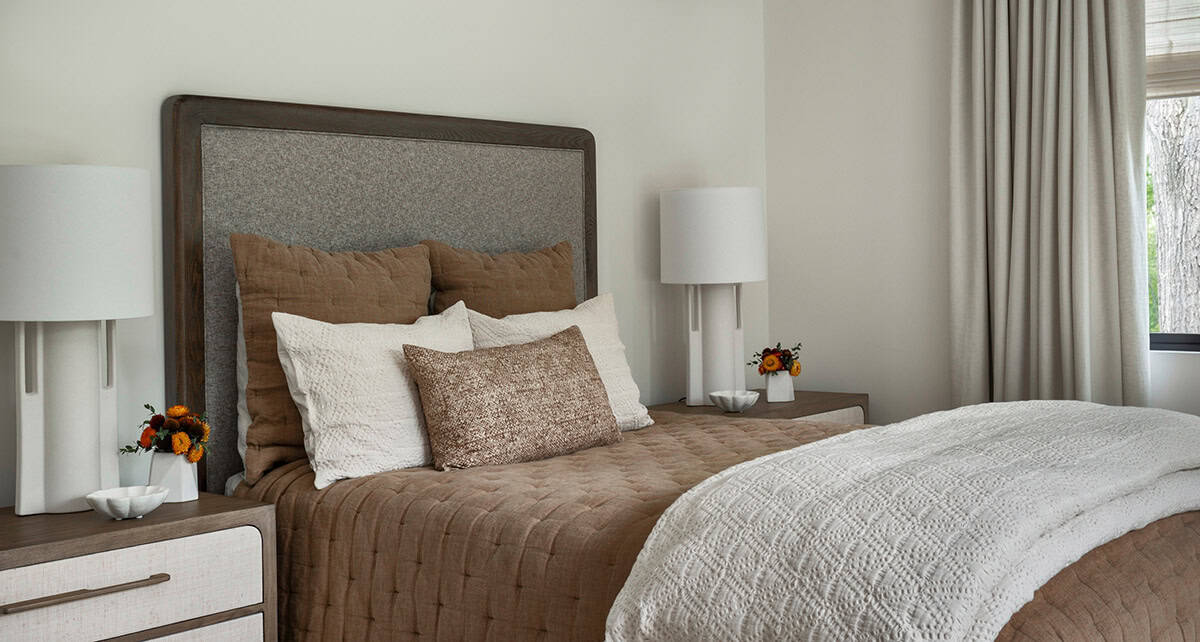 Bedroom with a gray upholstered headboard, brown quilted bedding, and white table lamps