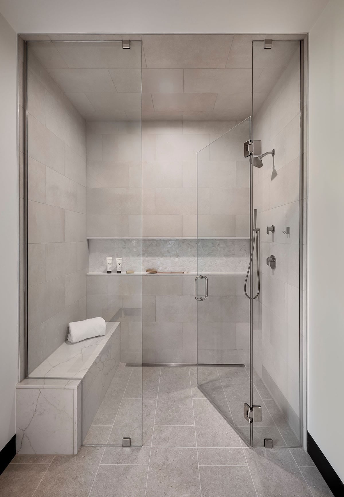 Walk-in shower with large gray tiles, a long niche, and a stone bench behind frameless glass