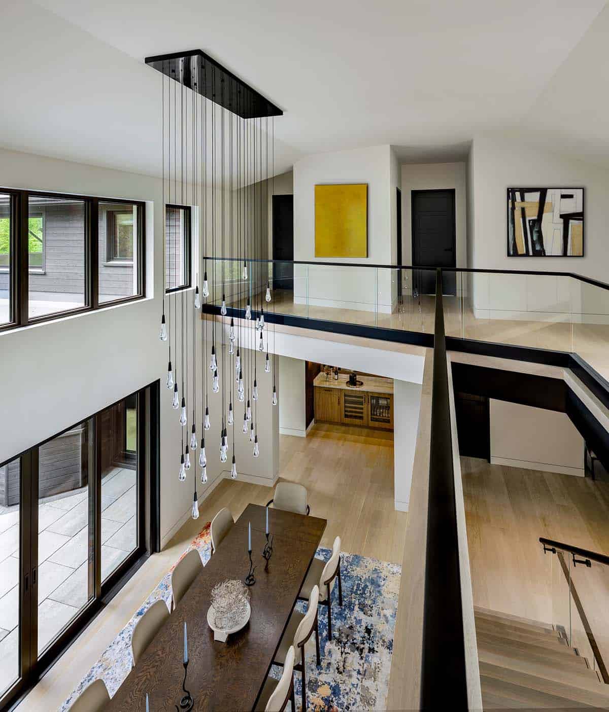 View from the upper landing past a glass drop chandelier to the dining table and wet bar below