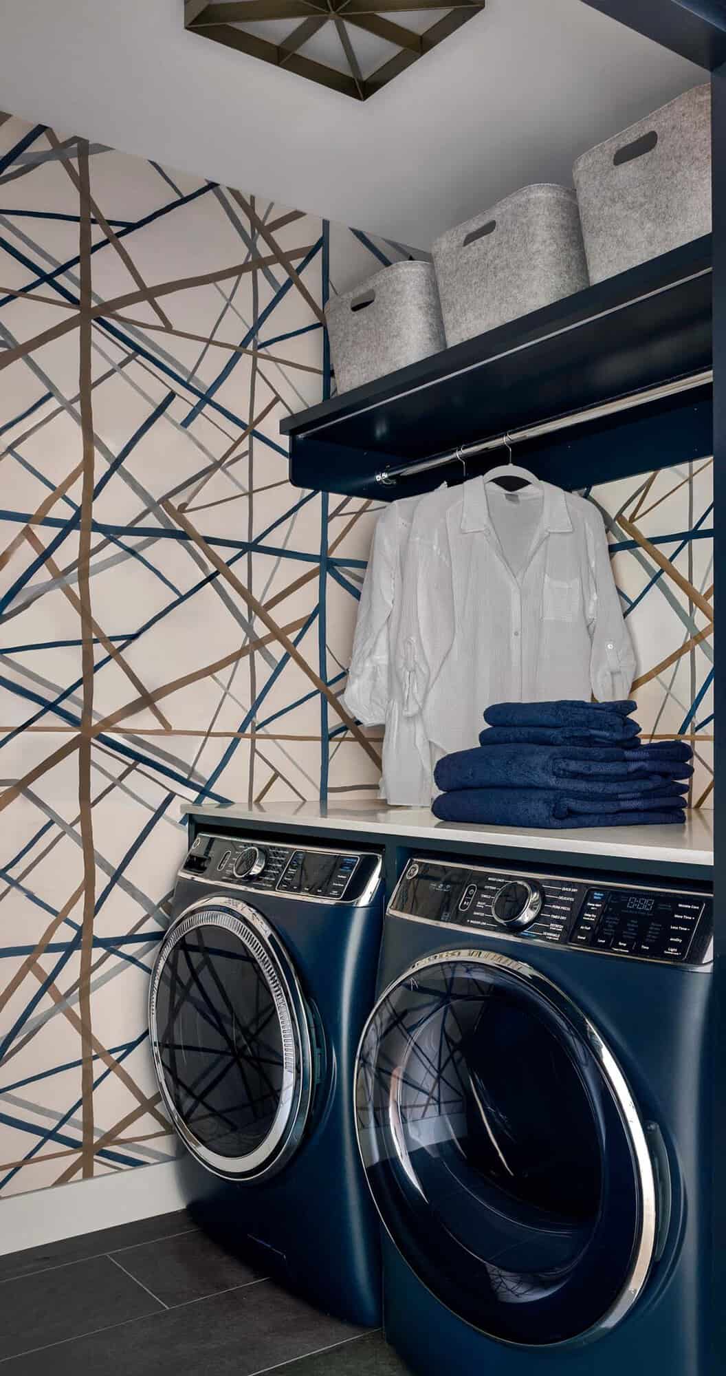 Laundry room with a navy washer and dryer, graphic line wallpaper, a hanging rod, and felt bins