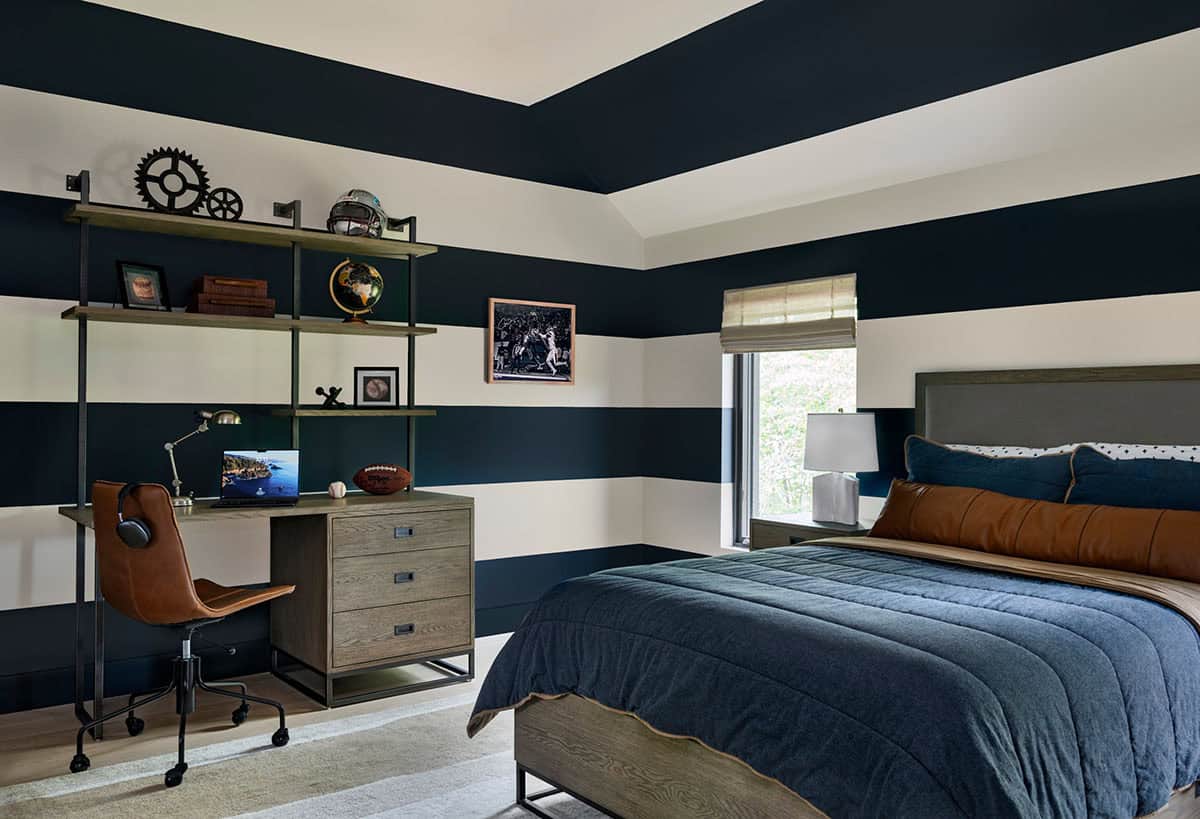 Bedroom with wide navy and white striped walls, a wall-mounted desk and shelves, and a navy comforter