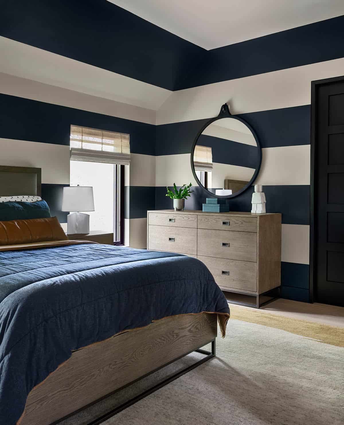 Navy and white striped bedroom with a gray oak dresser under a round black mirror