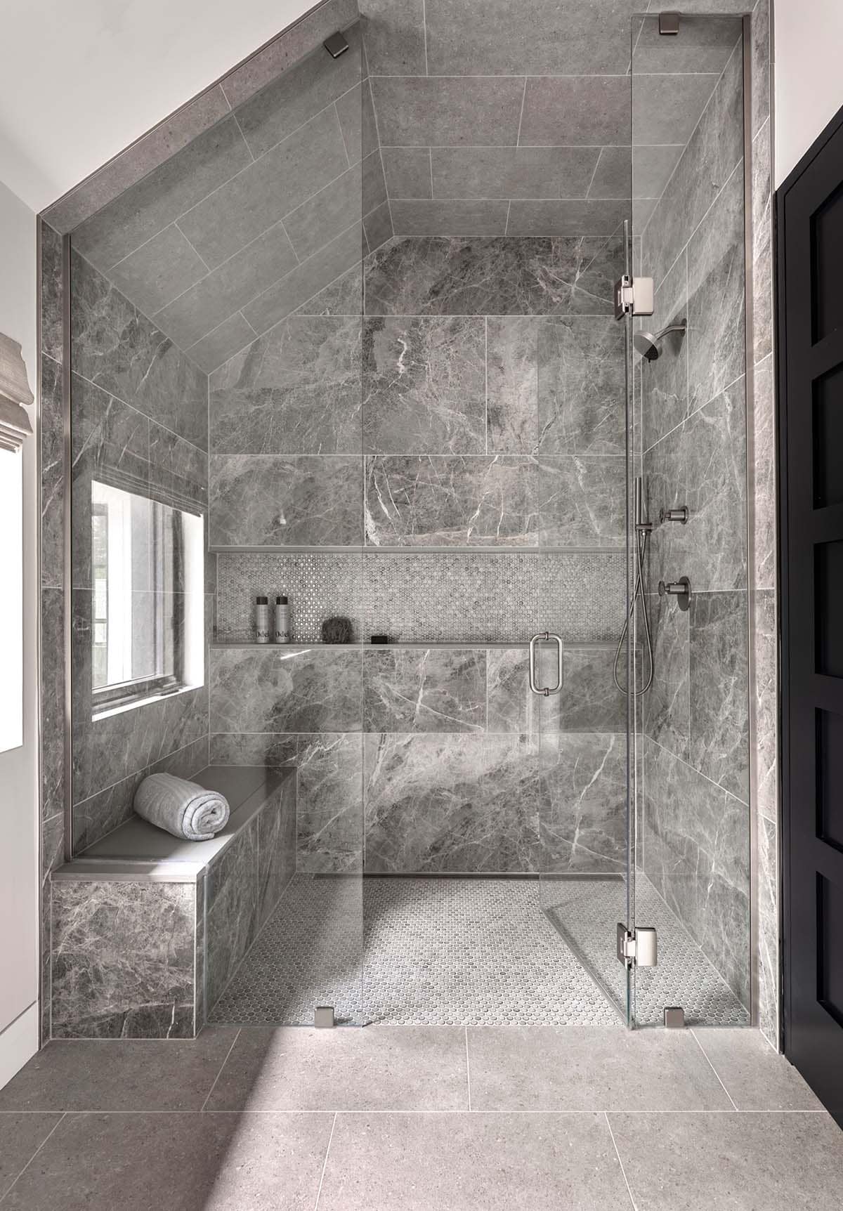 Shower under a sloped ceiling with gray marble tile, a penny tile niche and floor, and a bench