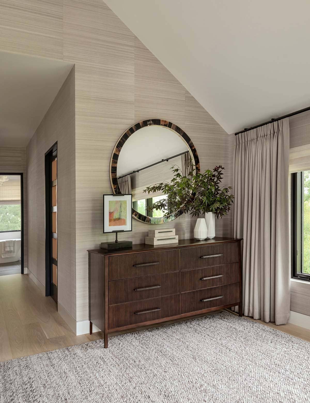 Fluted walnut dresser under a round horn-framed mirror, with a doorway through to the bathroom