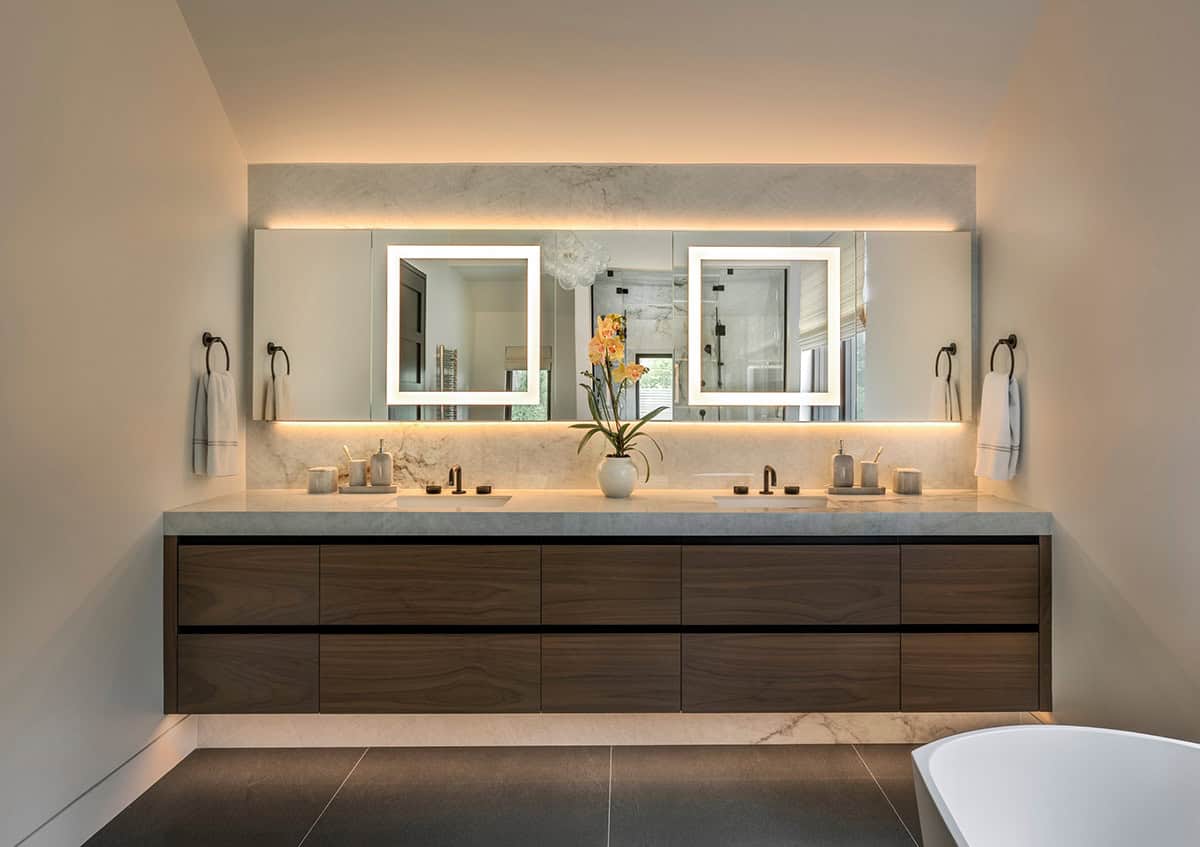 Floating walnut double vanity with backlit mirrors and a marble backsplash