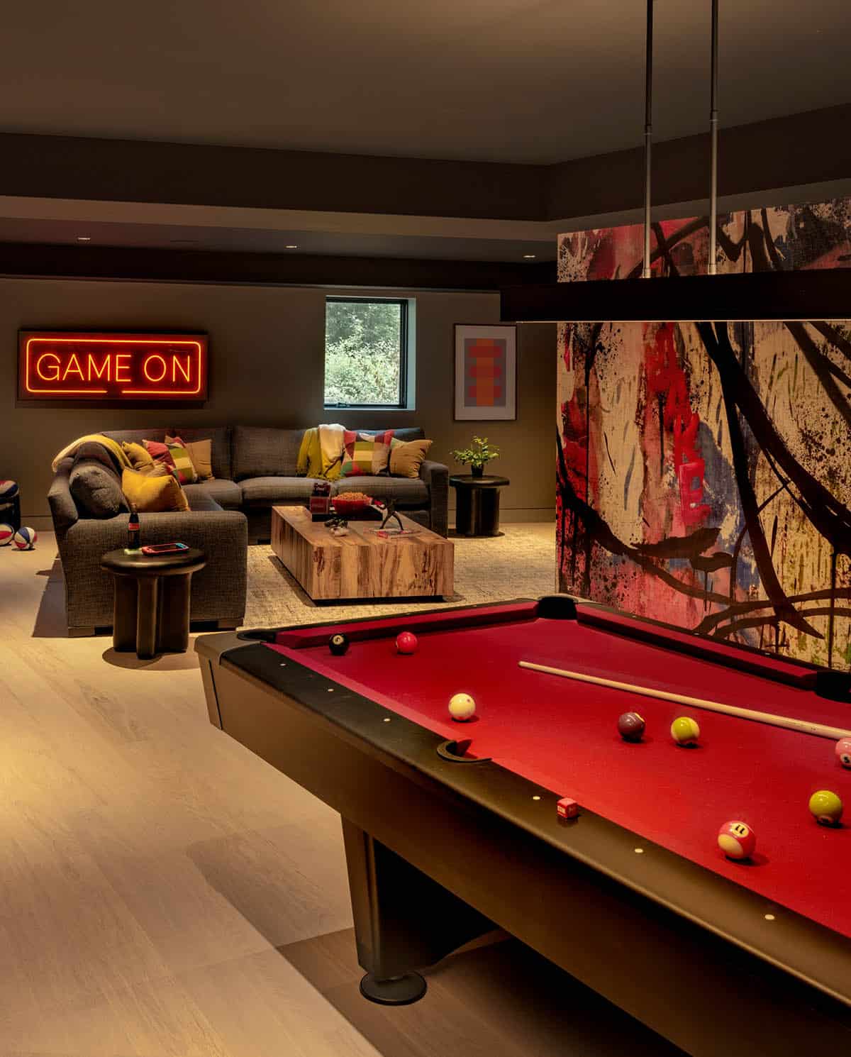 Red pool table beside a graffiti mural, with a sectional lounge under a neon Game On sign