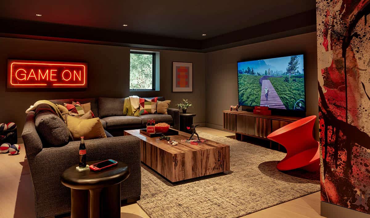 Lounge with a gray sectional, wood block coffee table, a TV showing a video game, and a red spinning chair