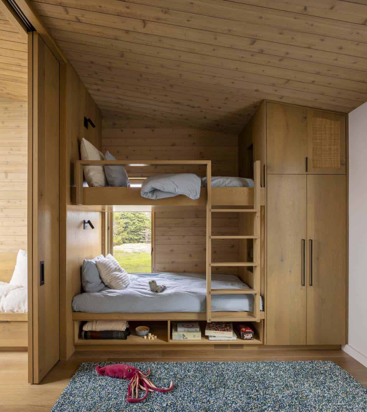 Built-in oak bunk beds with shelving, a wardrobe, and a small window, plus a plush squid toy on the rug