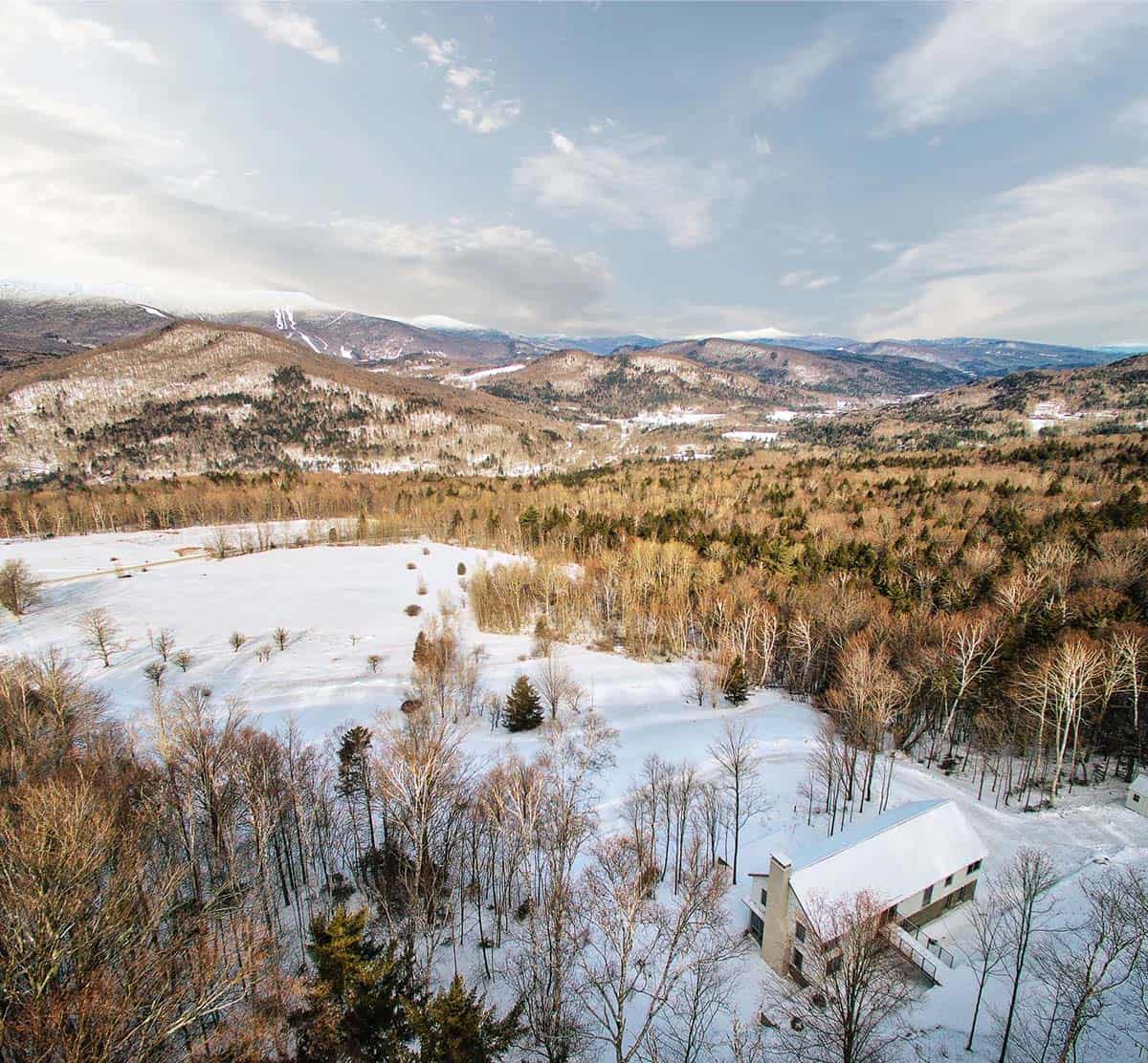 Aerial view of the home on a snowy hillside with mountains beyond
