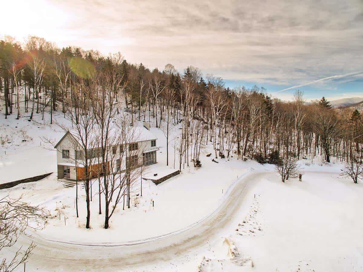 Snow-covered home in the woods beside a curving driveway