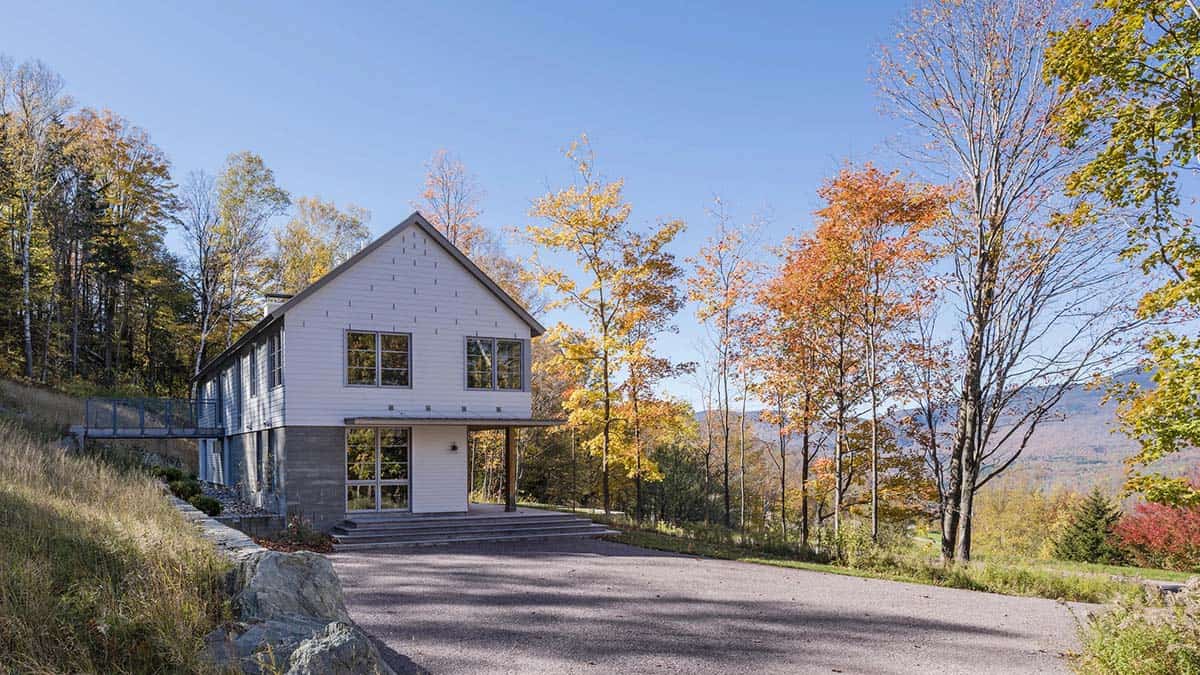 Gabled home with board-formed concrete base and bridge to hillside paths