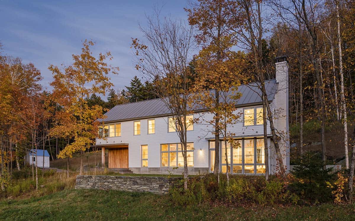 Home at twilight with warm interior light and a stone wall in front